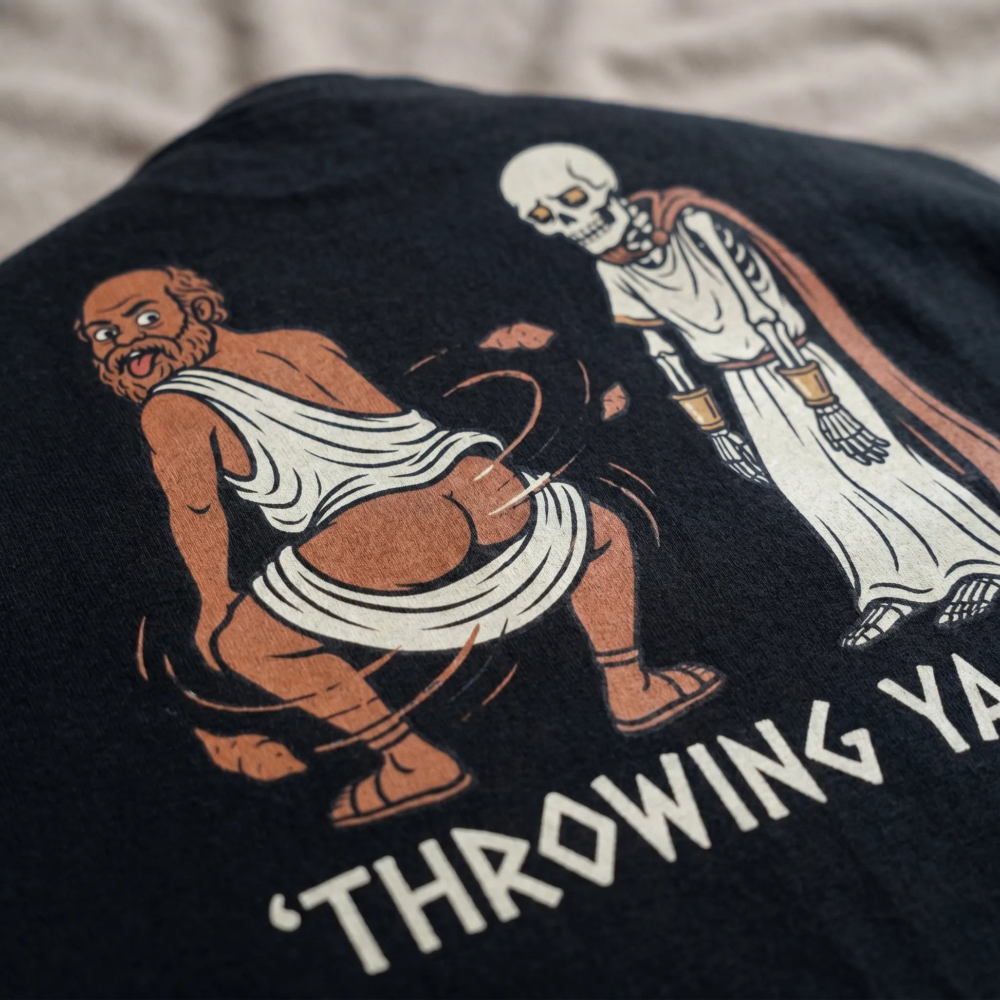 Close-up detail of the soft-hand DTG print on a Socrates Skeleton Tee, highlighting the AI-slop ragebait meme design of the throwing yams philosopher in a unisex fit.